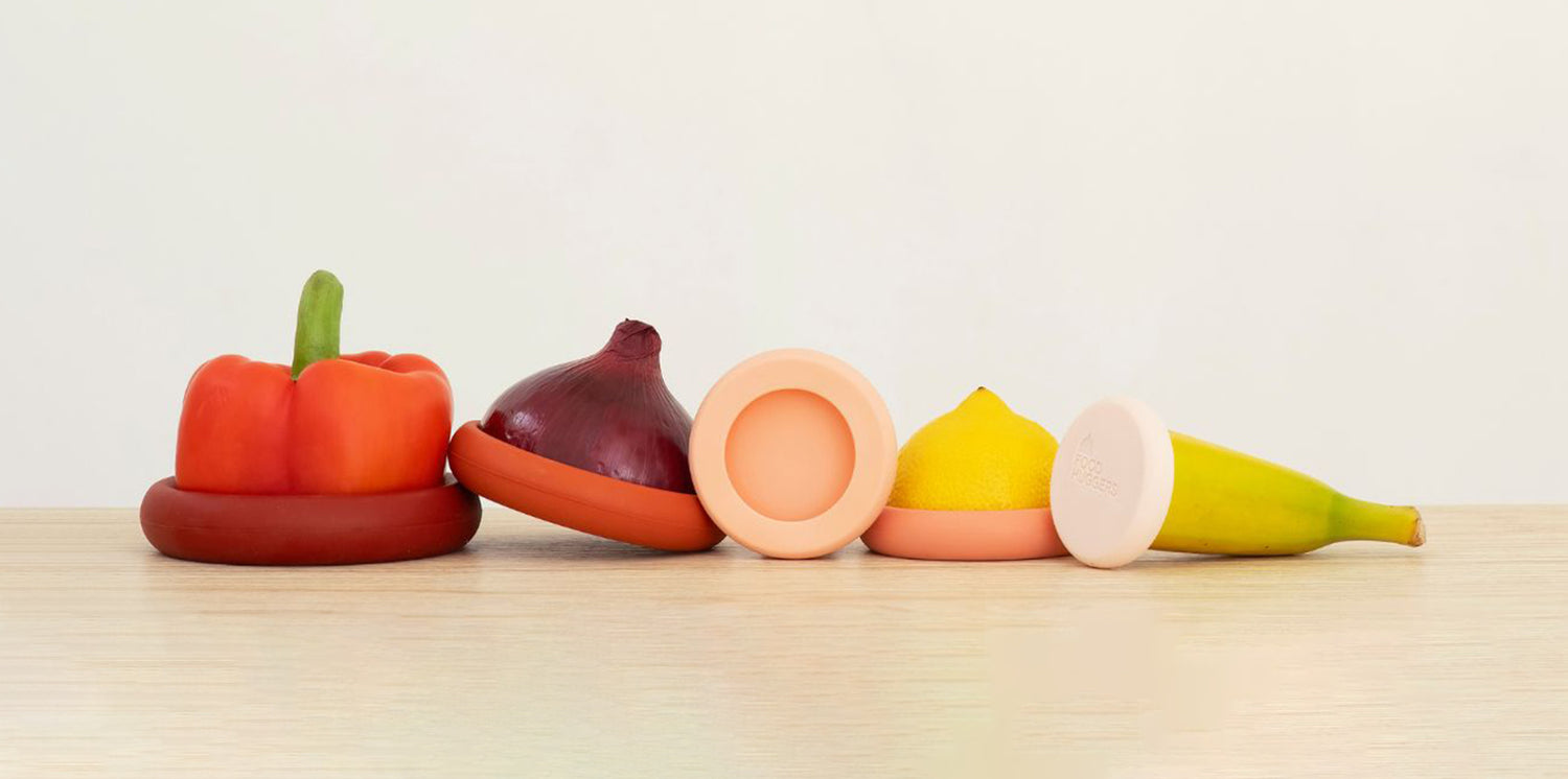 Five Food Huggers preserving fruits and vegetables, on a wooden table for sustainable kitchen